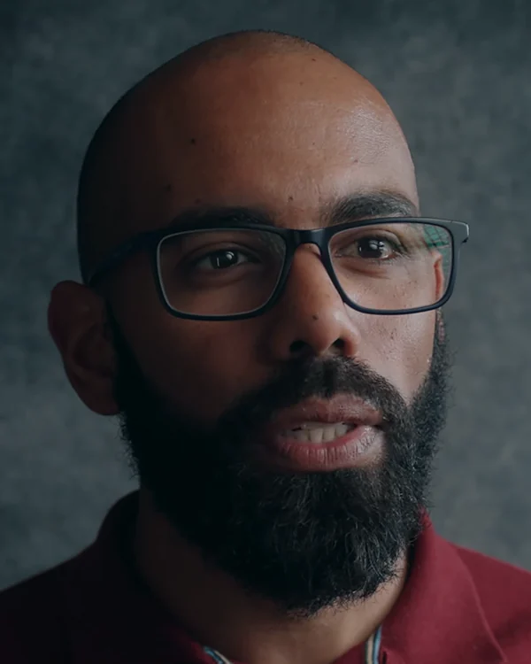 Leonardo Lemos in glasses and a burgundy shirt, speaking to the camera